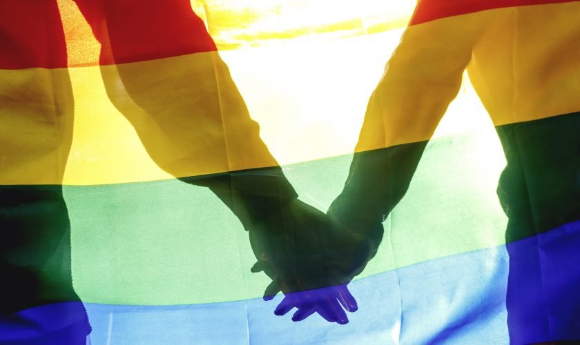 People, homosexuality, same-sex marriage, gay and love concept – close up of happy male gay couple hugging and holding rainbow flag